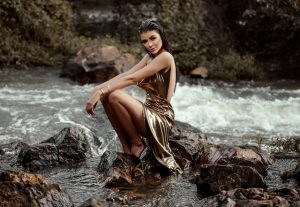 photo-of-woman-in-a-gold-gown-sitting-on-a-rock-in-the-river-2308368